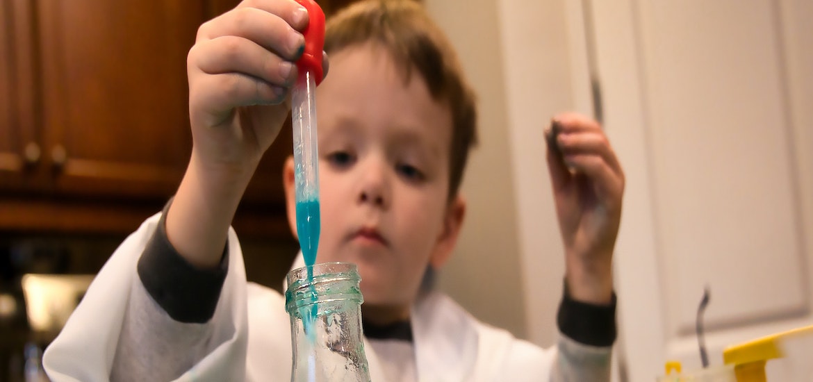 a small boy in a lab coat drops some liquid into a test tube