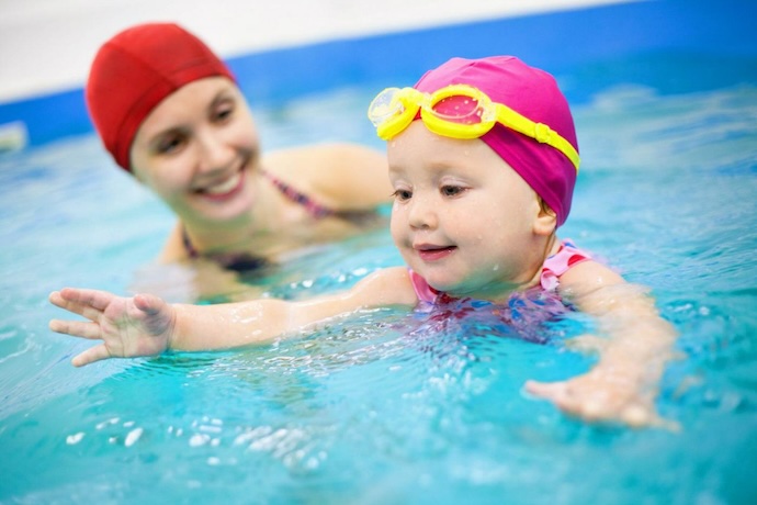Mother beside child swimming for the first time in a pool