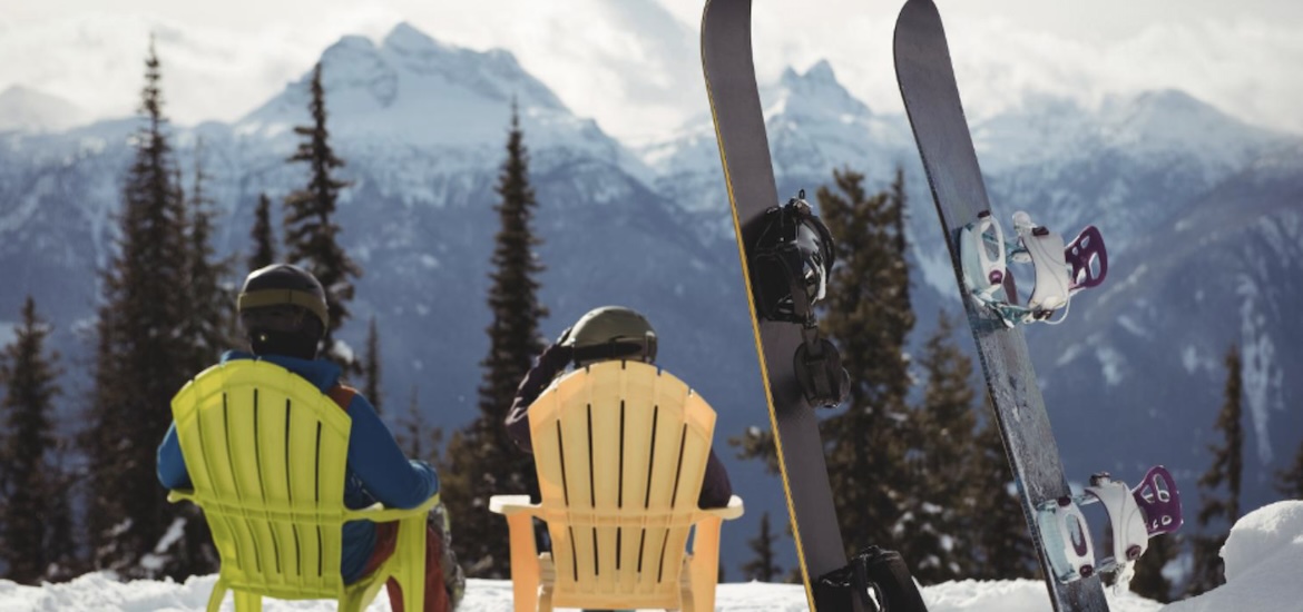 couple-sitting-chair-by-snowboards-snow-covered-mountain
