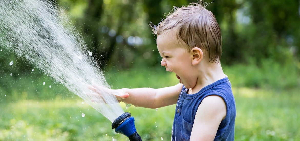 A toddler plays with a hosepipe