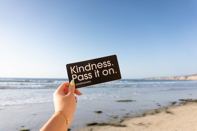 a hand holding a kindness pass it on sign