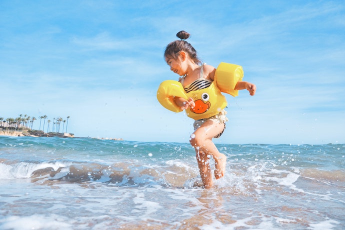 a small girl wearing a rubber duck life savers plays in the sea