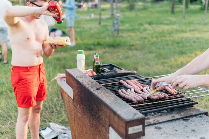 sausages grill on a bbq and someone adds ketchup to their hot dog