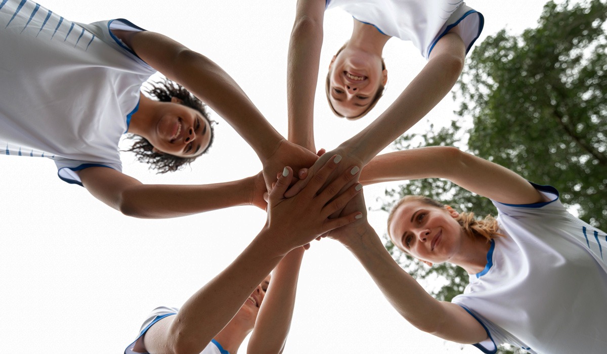 Female cheerleaders huddle hands together smiling outdoors