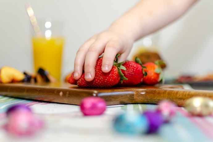 a child's hand grabs strawberries from a snack board