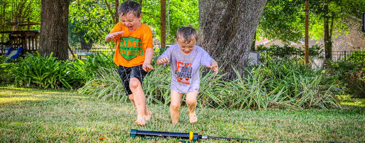 two boys play in a water sprinkler