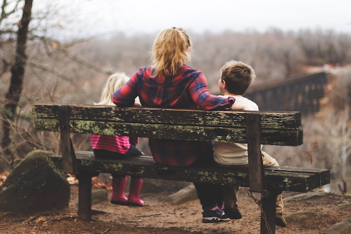 a mum and two kids sit on a bench in nature