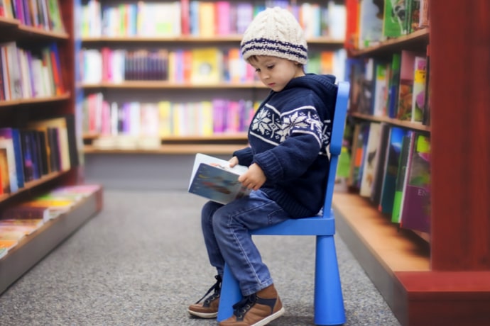 Adorable little boy, sitting in a book store, looking at books