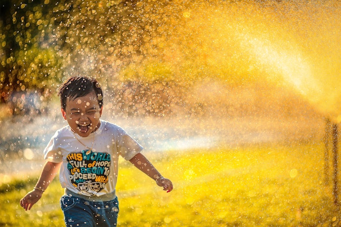 a boy runs through a sprinkler laughing