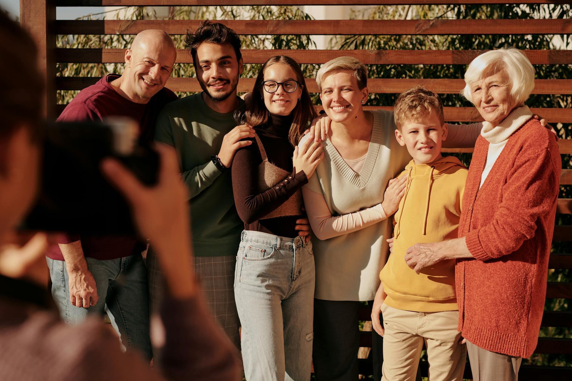A multi-generational family smiling warmly outdoors while someone in the foreground takes their photograph