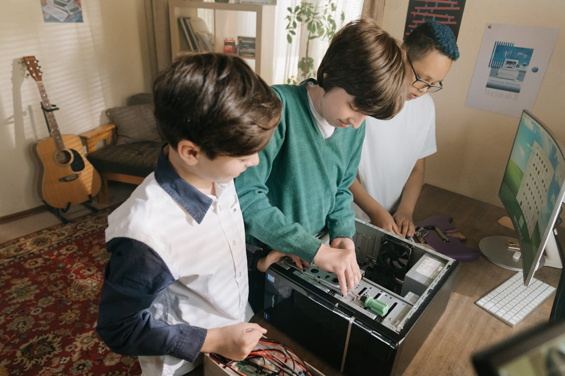 Three children learning to fix a computer, looking inside the case using tools
