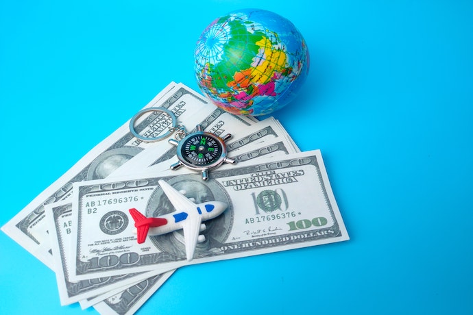 a stack of money, a compass and a toy plane suggest travel