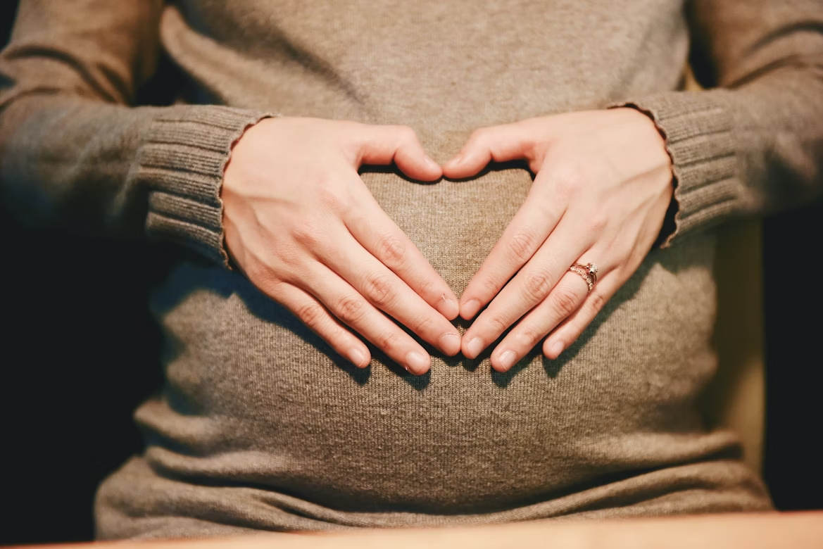 A pregnant woman forming a heart with her hands over her belly.