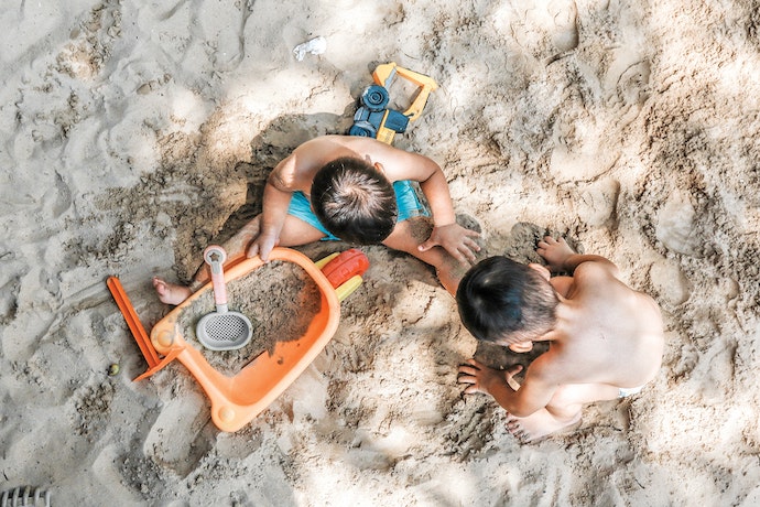 2 boys [play in the sand with a wheelbarrow and spades