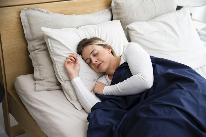 A woman peacefully sleeping in a bed with white pillows and a navy blue blanket.