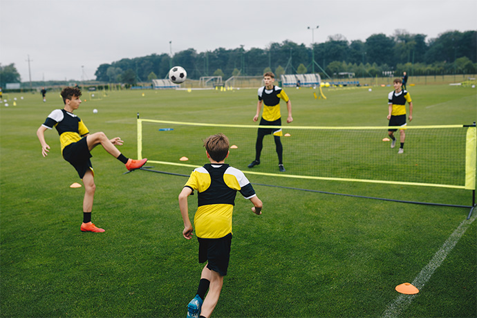 4 boys play soccer over a net like tenis