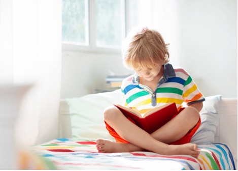 Child wearing bright colors reading on his bed