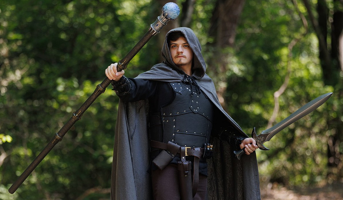 ALT Text: Cloaked fantasy warrior with staff and sword