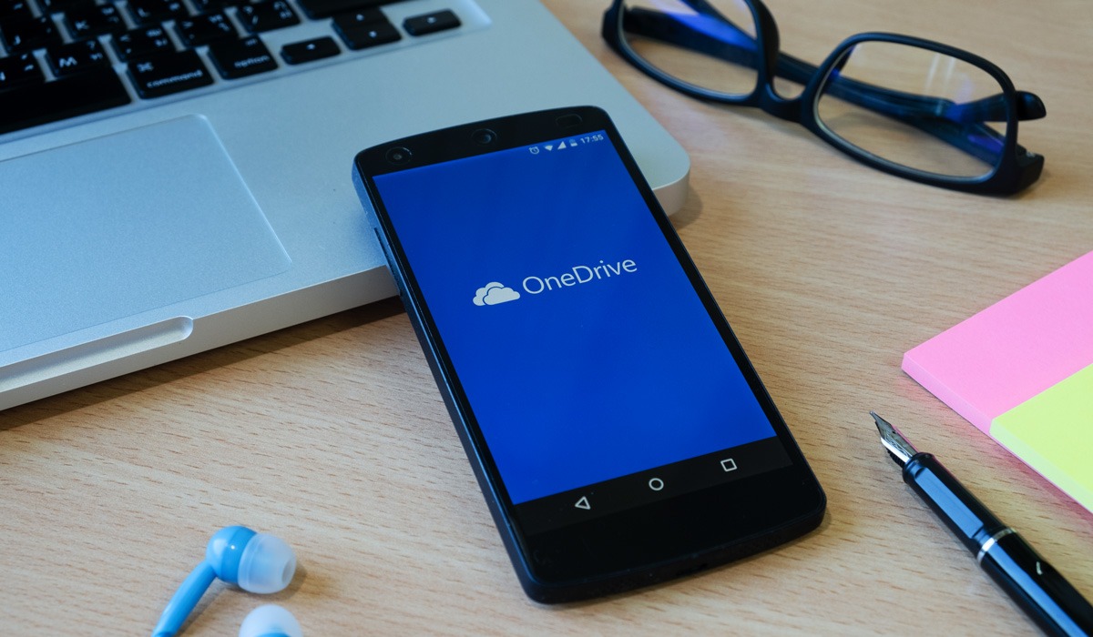 Smartphone displaying OneDrive app next to laptop and glasses