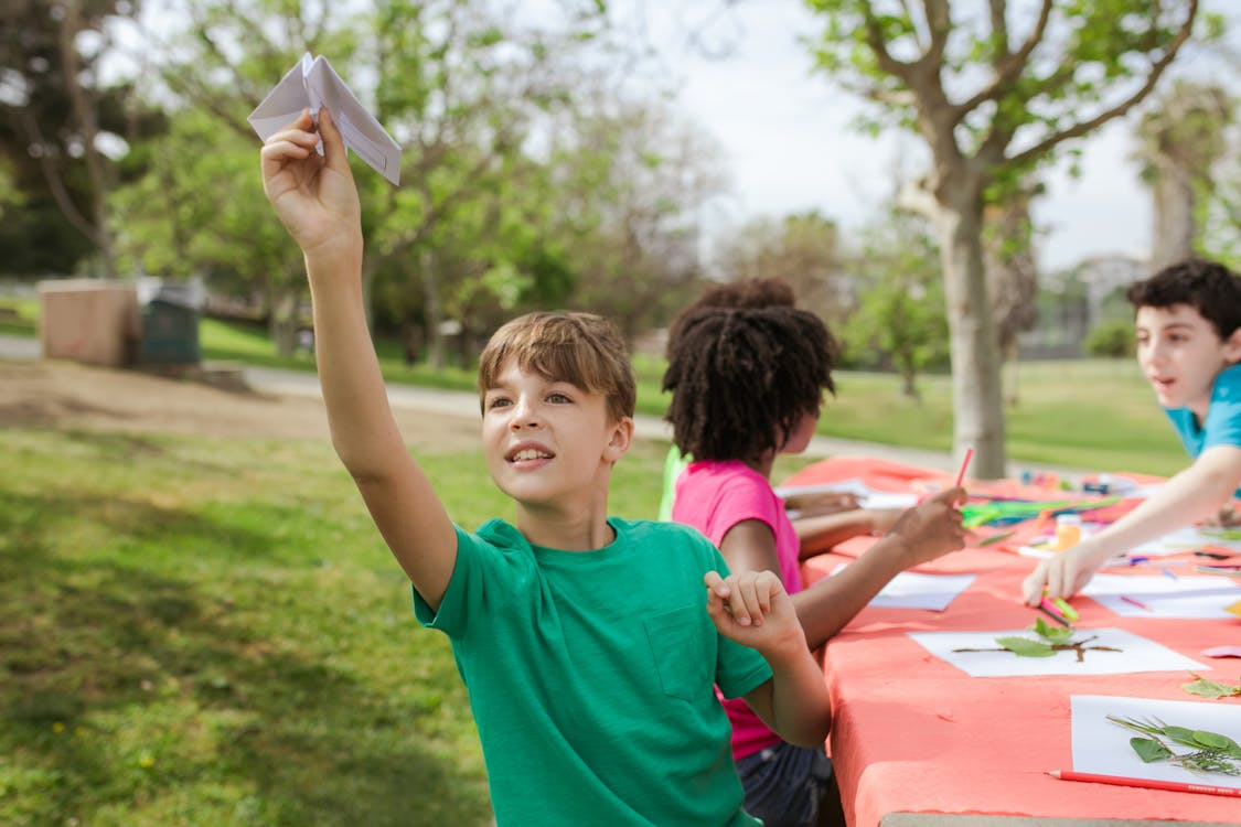Children at table outdoors carry out fun summer project involving leaves and paper planes