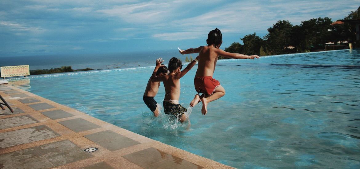 three boys jump in pool