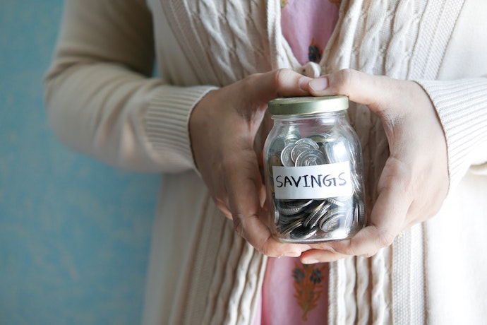 a hand holds a jar of coins saying savings
