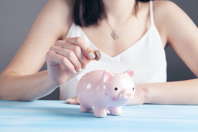 a woman puts money into a pink piggy bank