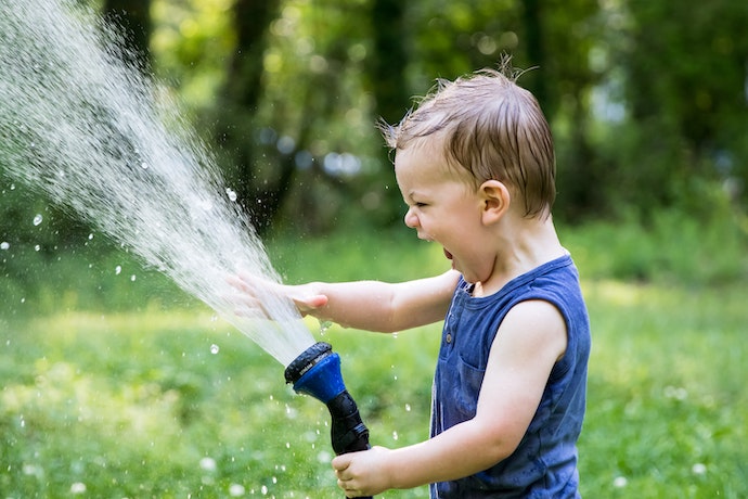 A toddler plays with a hosepipe
