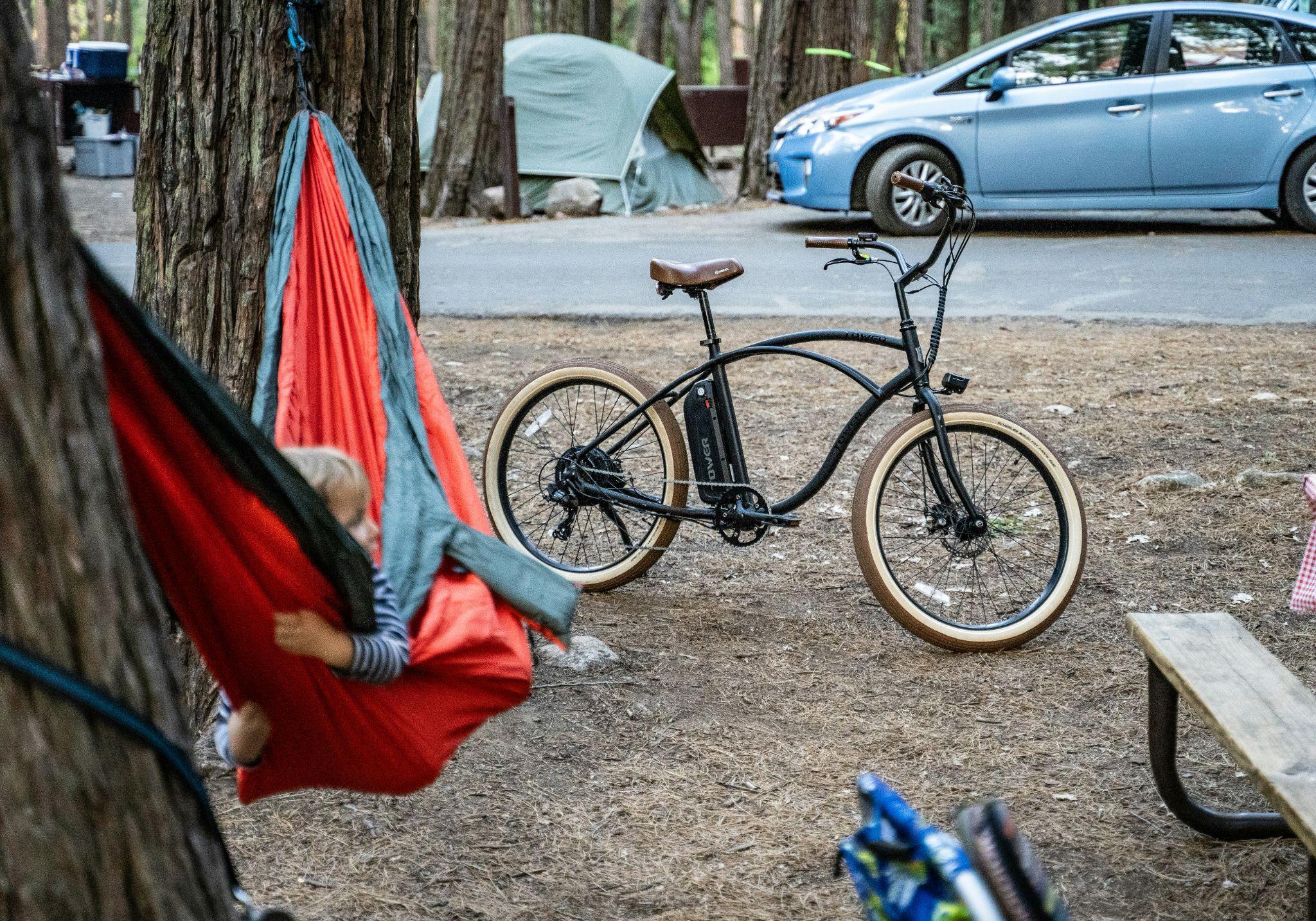 Child relaxing in a hammock at a forest campsite with a bicycle nearby