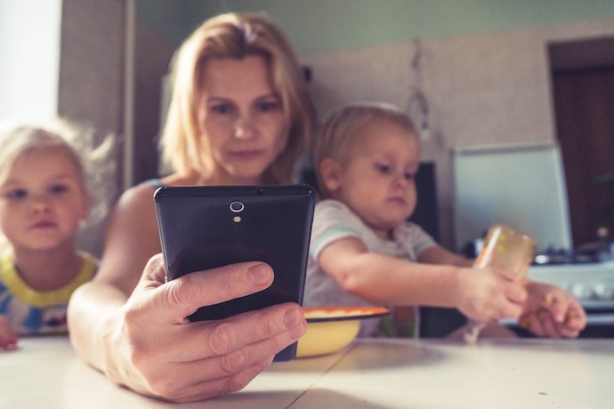 a mom juggles a smart phone and two kids