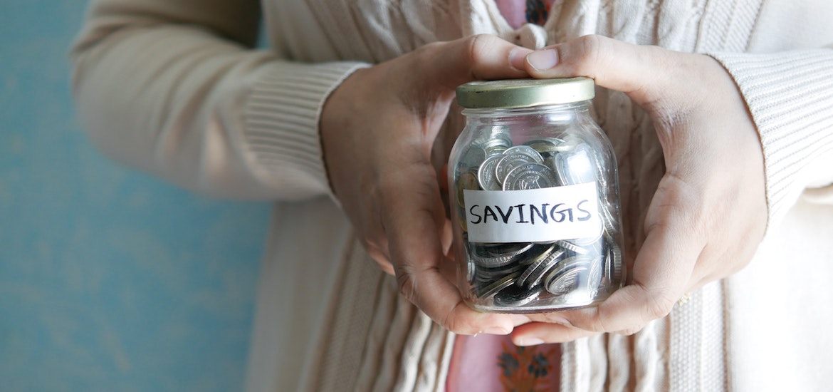 a hand holds a jar of coins saying savings