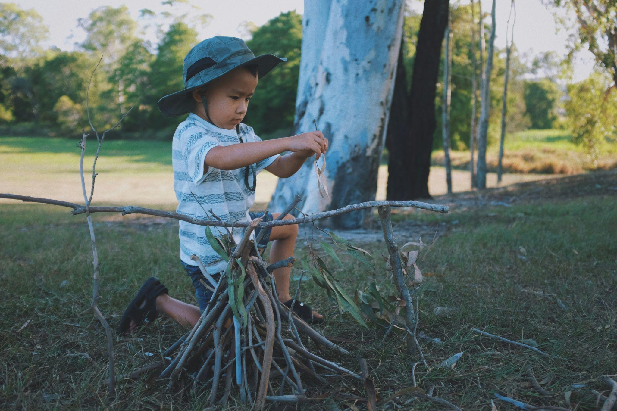 Child building a small stick structure outdoors in a forest