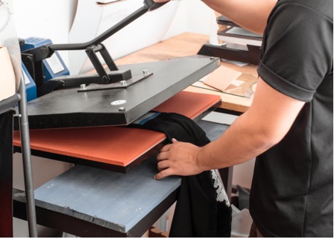 Person operating a heat press machine to apply a design onto a shirt.