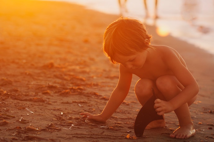 a small boy plays in the sand at sunset