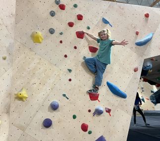 Girl climbs red climbing holds to top of wall