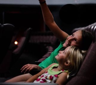Two children sitting in planetarium seating, pointing up at the ceiling