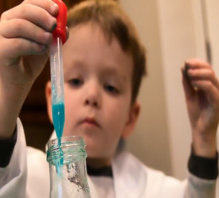 a small boy in a lab coat drops some liquid into a test tube