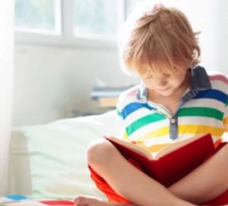 Child wearing bright colors reading on his bed