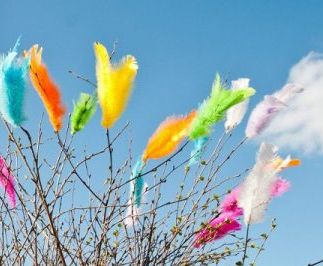 Twigs decorated with colorful feathers, blue sky in background