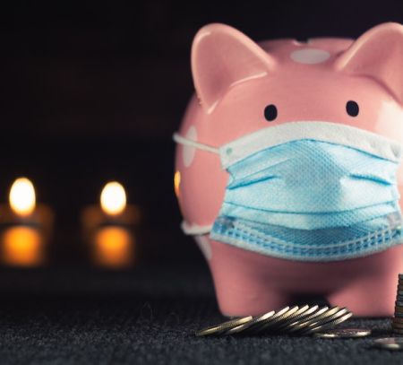a piggy bank with a covid mask near a pile of change