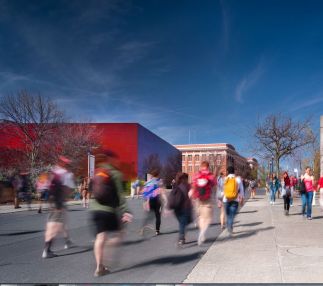 A mirrored red glass building with students walking uphill on a college campus