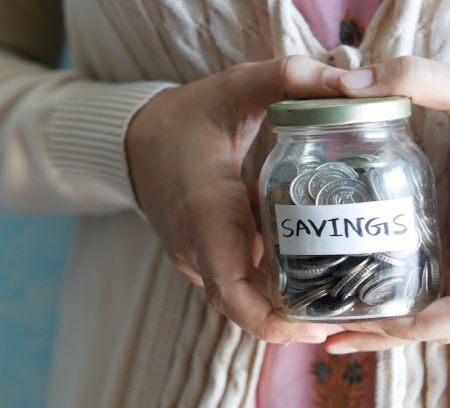 A ladies hand hold a jar of savings