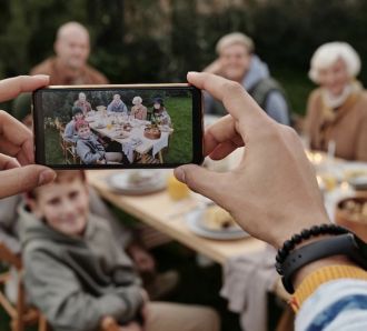 Hands holding a smartphone to take a photo of a multi-generational family enjoying a meal together at an outdoor table