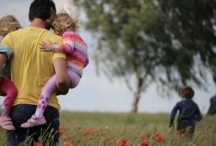  A man carries two children through a field of red flowers, with another child running ahead.